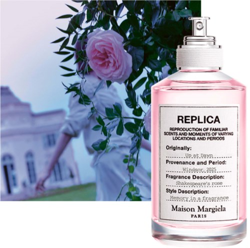 Ein Parfümflasche mit dem Label Replica und rosa Flüssigkeit vor einer Person mit Blumen und einem Gebäude im Hintergrund.