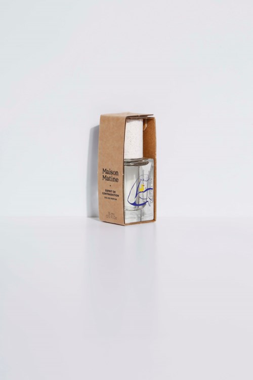 A clear bottle with a splash of yellow and blue juice, inside a cardboard box labeled 'Maison Matine'.