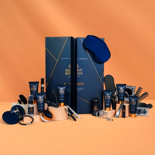 A collection of men's skincare and grooming products arranged around a blue gift box with a calendar and blue eye mask.