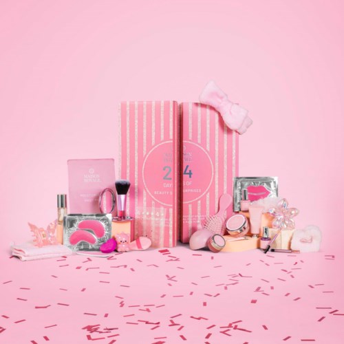 Beauty and skincare products, brushes, and accessories arranged on a pink background with confetti and a pink striped box.