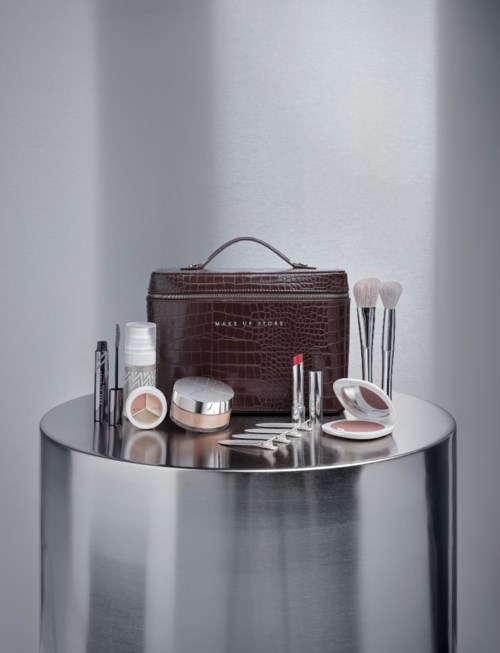 Makeup brushes, compact powder, lipstick, foundation, and a brown makeup bag arranged on a round metallic surface.