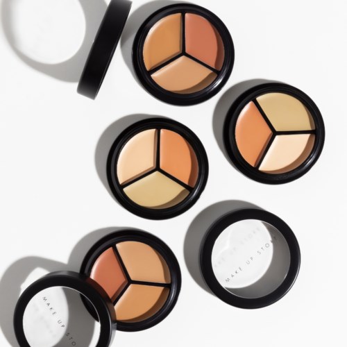 Ronde make-up containers met crème blush en poeder, sommige open en sommige gesloten, werpen schaduwen op een witte achtergrond.