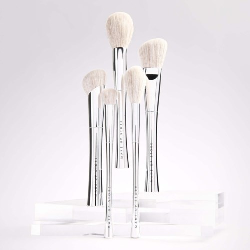 Set of six white makeup brushes with silver handles on a white display stand.