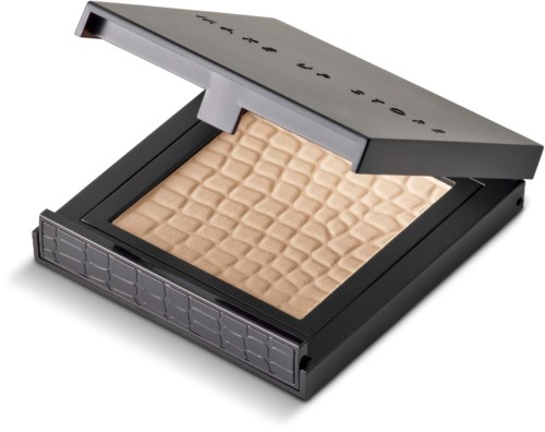 En sminkkompakt med beige puder och ett svart- och silverfodral, delvis öppet, som visar texturerat puder inuti.