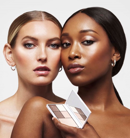 Twee vrouwen met verschillende huidtinten houden een make-up palet vast, dicht bij elkaar, kijken naar de camera.