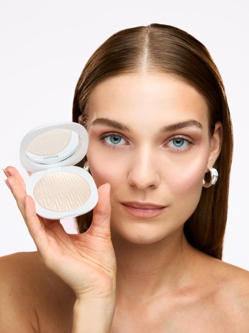 Woman with brown hair holding a compact powder with a mirror inside, looking at the camera.