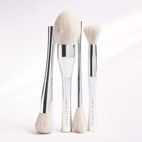 Three makeup brushes with silver and white handles are shown, varying in size and shape.