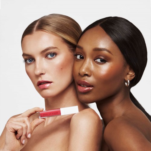 Twee vrouwen met verschillende huidtinten houden een lippenstift en poseren dicht bij elkaar voor een foto.