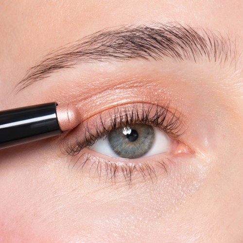A close-up of a person putting on light-colored eyeshadow with a makeup brush.