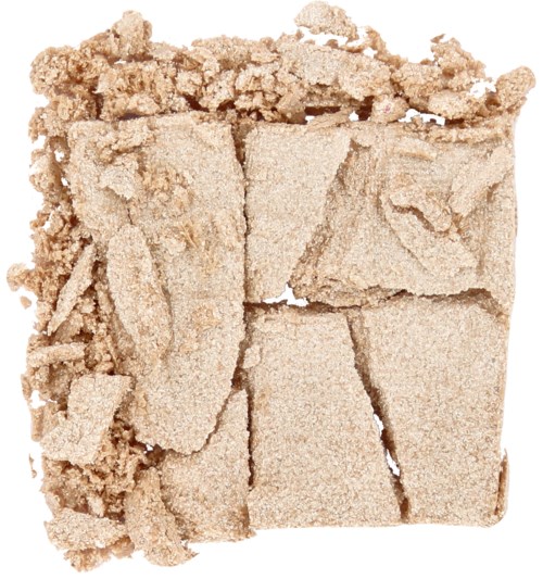 Ett krossat pulver eller block, beige färg med ojämna, brutna bitar och lösa gryn omkring.