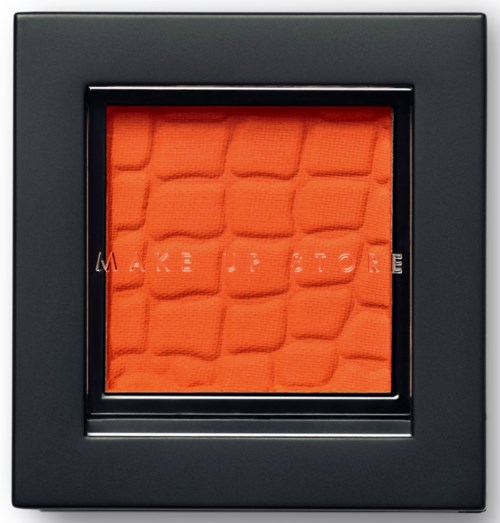 En orange texturerad yta inuti en svart ram med delvis synliga bokstäver: 'MAKE', 'UP', 'STORE' och 'ME'.