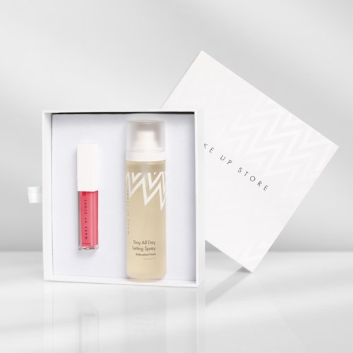 Een witte doos met lippenstift en fixing spray erin, naast een witte en grijze doos met tekst.