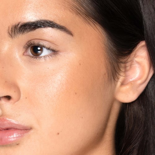 Close-up van het gezicht van een vrouw met een heldere huid, een bruin oog en deel van de neus en lippen.