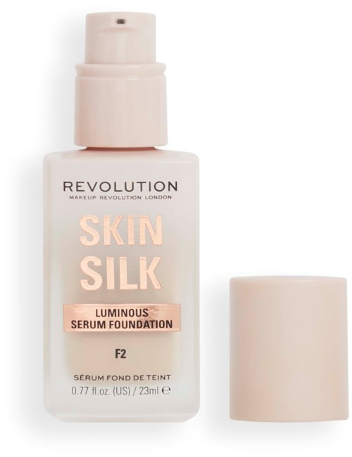 A white foundation bottle labeled 'Revolution Skin Silk Luminous Serum Foundation' with a cap beside it.