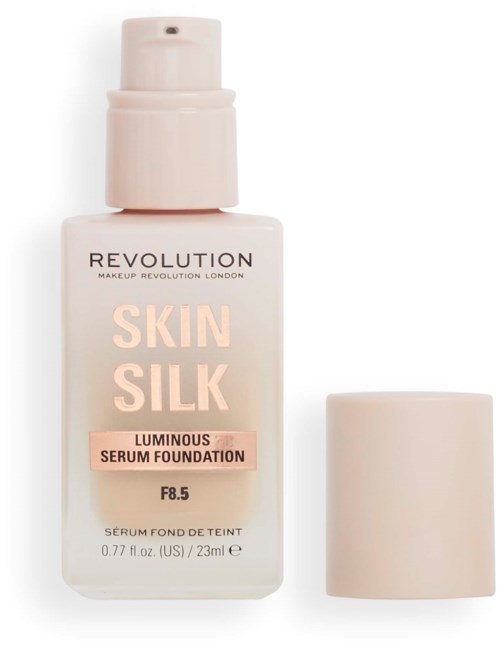 A bottle of Revolution Skin Silk luminous serum foundation with pink lettering, and its cap placed beside it.