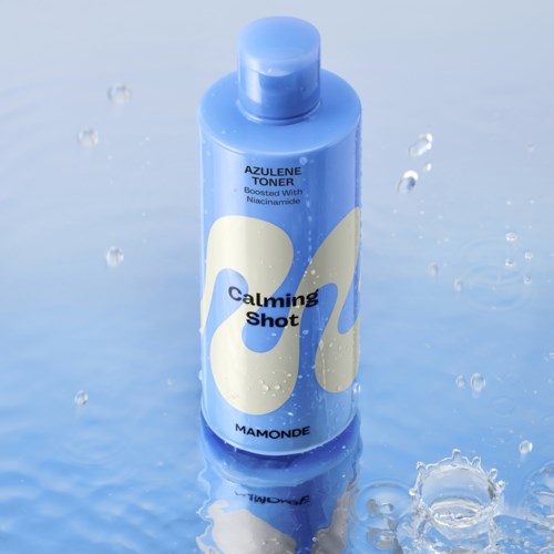Een blauwe fles met 'Calming Shot' erop, waterdruppels eromheen en een reflecterend oppervlak.