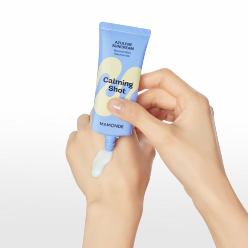 Hand drückt auf eine blaue Tube mit 'Calming Shot' und weißer Creme kommt heraus.