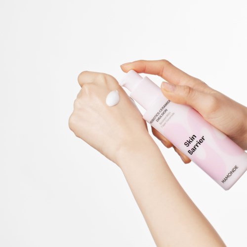 Iemand brengt een witte crème aan met de tekst 'Skin Barrier' op de hand tegen een witte achtergrond.