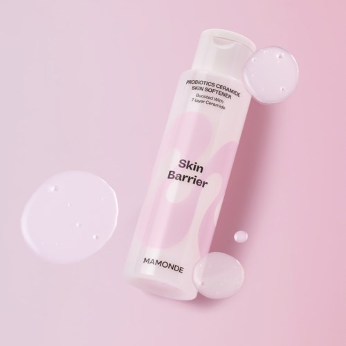 Een huidverzorgingsproduct genaamd Skin Barrier van Mamonde, met roze en witte verpakking, omgeven door heldere bollen op een roze achtergrond.