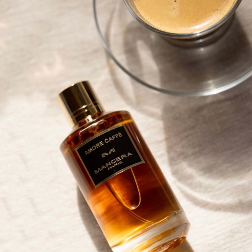 Een flesje Amore Caffé Mangera Paris parfum ligt op een oppervlak, met een drankje in de buurt.