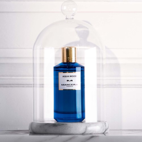 Blauwe fles met 'Aqua Wood' onder glazen stolp met marmeren voet. Minimalistisch en stijlvol.
