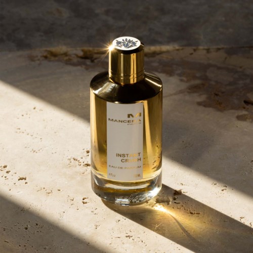 Een gouden fles huidverzorgingscrème op een lichte ondergrond met schaduw van zonlicht.