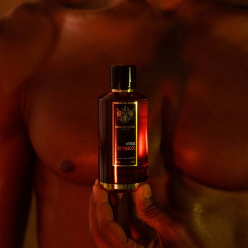 Een hand houdt een fles geur met label 'Intense Red Tobacco', met gespierde torsos op de achtergrond.