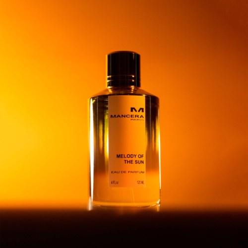 Een parfumfles staat voor een oranjegele gradient achtergrond, gelabeld "MANCERA" met de geur "MELODY OF THE SUN."