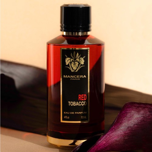 Een rood parfumflesje met zwart deksel, label en gouden ontwerp, geplaatst op een donkere paarse stofachtergrond.