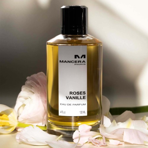 Een parfumfles met de label 'ROSES VANILLE' omgeven door roze en witte bloembladeren.