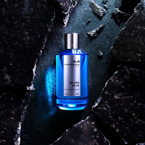 Een blauw parfumflesje met label 'Silver Blue' van Mancera, tussen zwarte stenen met een moderne uitstraling.