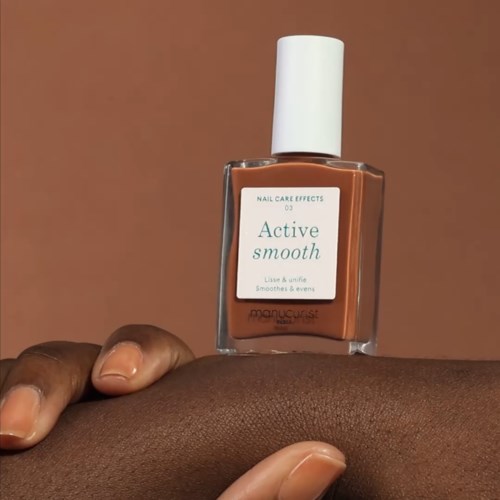 A hand holds a brown nail polish bottle labeled "Active Smooth" against a plain background.
