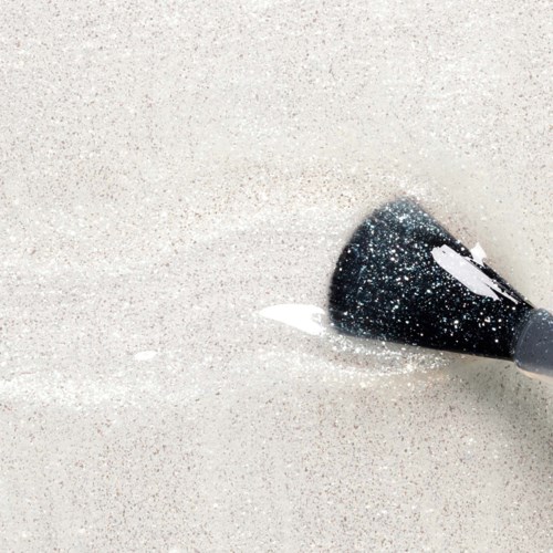 Makeupkost med svarte bust og glitter, ligger på en sandete overflate nær noen sølt hvit pigment.