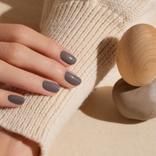Hand with gray painted nails resting on a cream-colored knit fabric, near stacked wooden and stone spheres.
