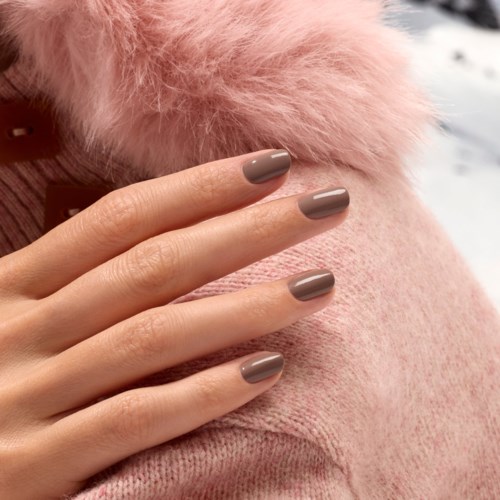 Manicure with neatly painted beige nails on a hand resting on a pink fuzzy fabric.