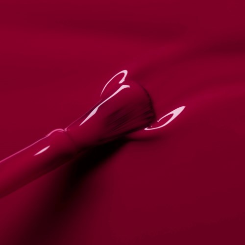 A red lipstick with a shiny surface lies on a matching red background.