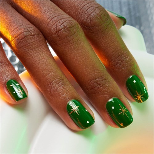 Festive green nail polish with golden Christmas star and bow designs on nails.