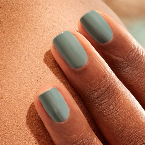 Three fingernails painted in light blue rest on a sandy surface.