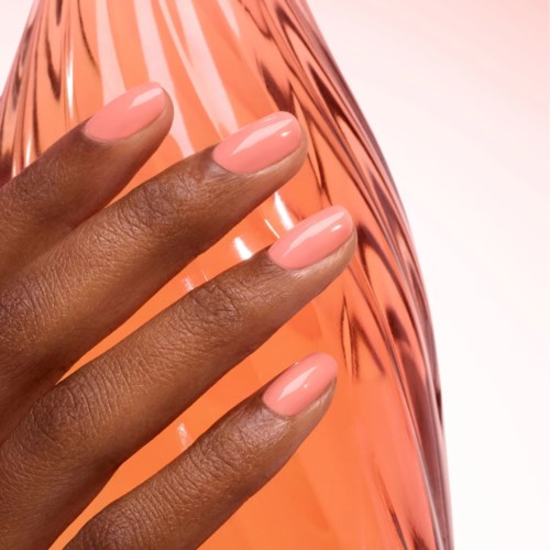 Close-up of a hand with neatly manicured nails in light pink polish, against a shiny, rose gold background.