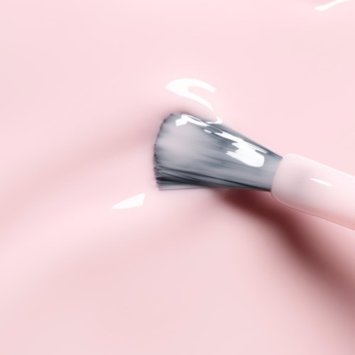 A makeup brush applies white cream on a pink surface.