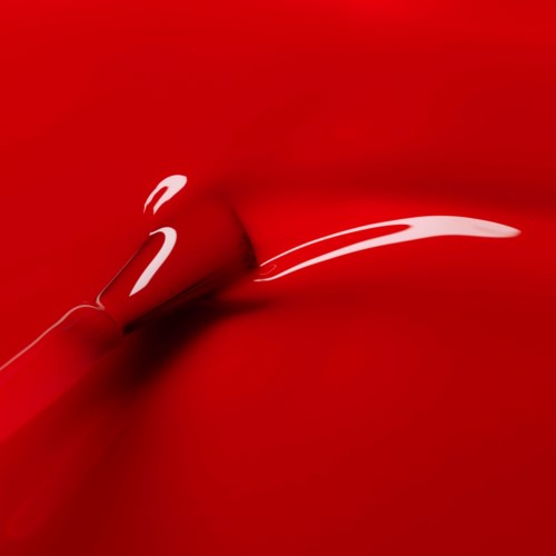 A red lipstick is shown, with the lipstick tip touching and creating a shiny streak on a red background.