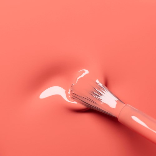 A brush with white liquid, possibly cream or paint, spreads on a peach-colored background.