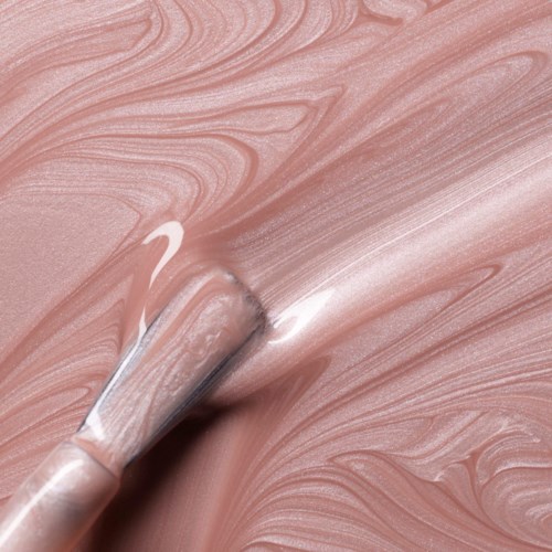 A brush spreads pinkish cream across a surface with swirling patterns.