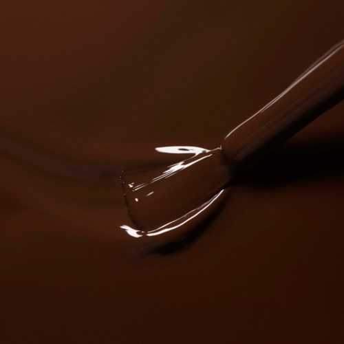 A paintbrush is mixing or spreading dark brown or chocolate-colored paint smoothly.