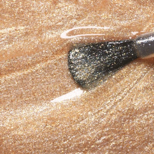 En makeupborste stryker ut skimrande guldögonskugga på huden med mjuka, blandade drag.