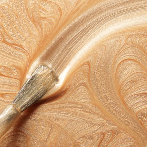 Bilden visar en pensel som applicerar beige färg med virvlande mönster på en yta.