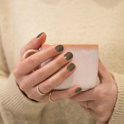 A hand holding a large ceramic mug with a person's nails painted dark green.