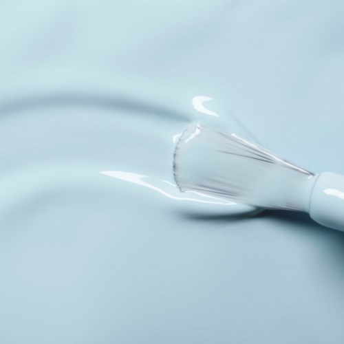 A glass dropper lying on a light blue surface, with some liquid inside, creating ripples.