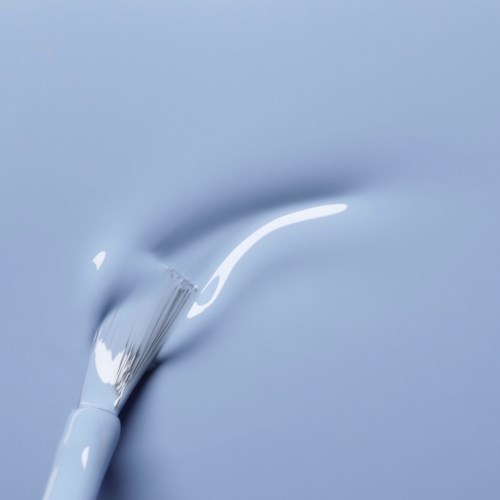 A paintbrush with white paint being applied to a light blue surface.