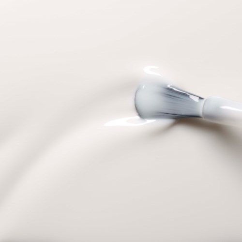 A white object, possibly a beauty or skincare device, lies on soft, smooth white surface with subtle shadows.